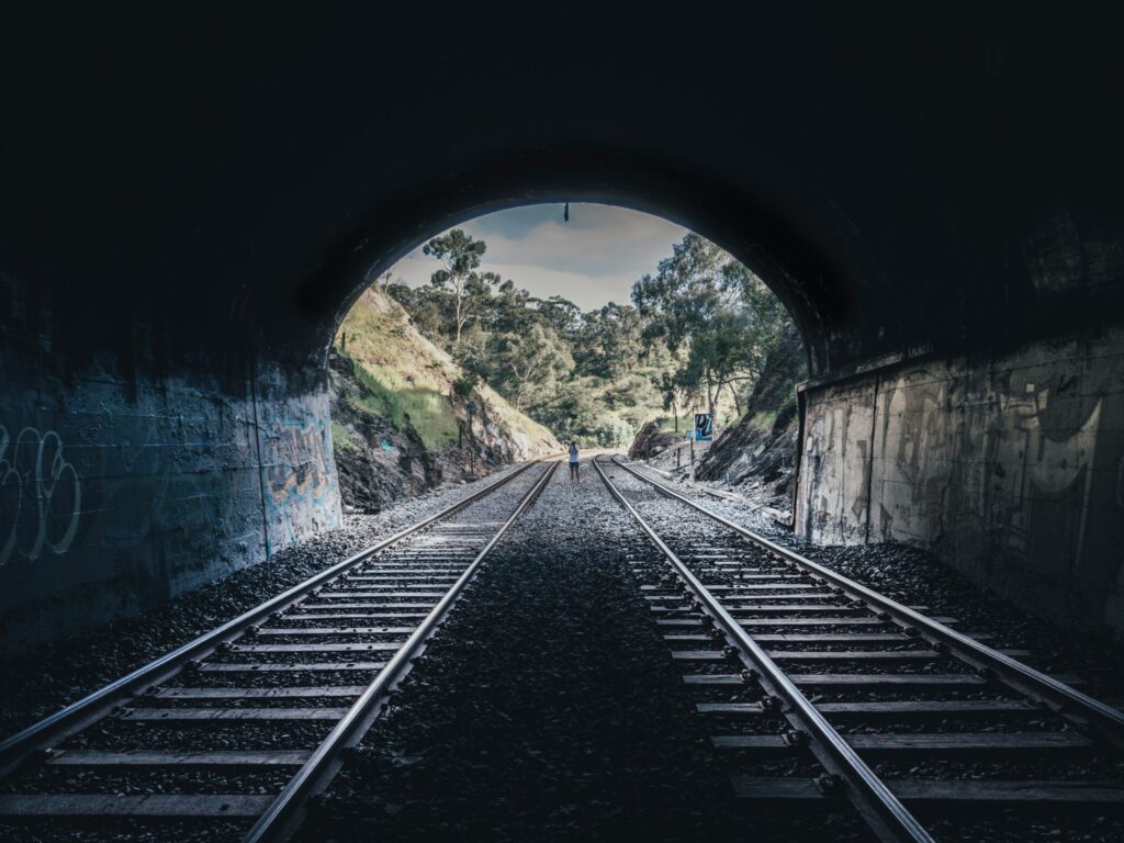 Two railroad diverging out of a tunnel with a person in the middle